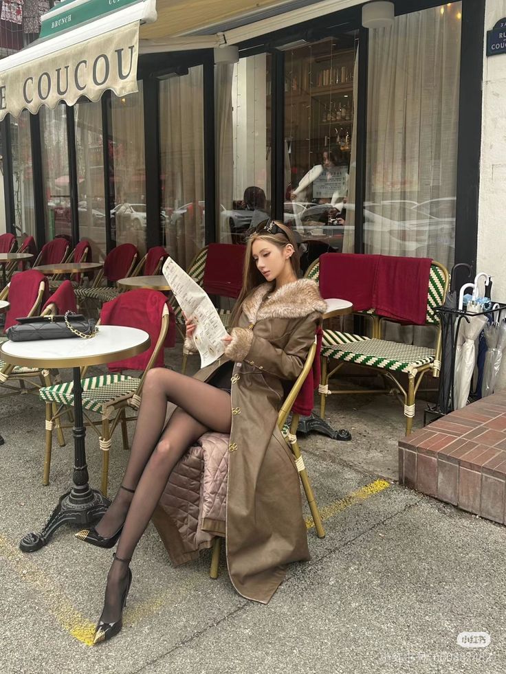 Woman in a long fur-collared coat and black tights sitting at an outdoor cafe