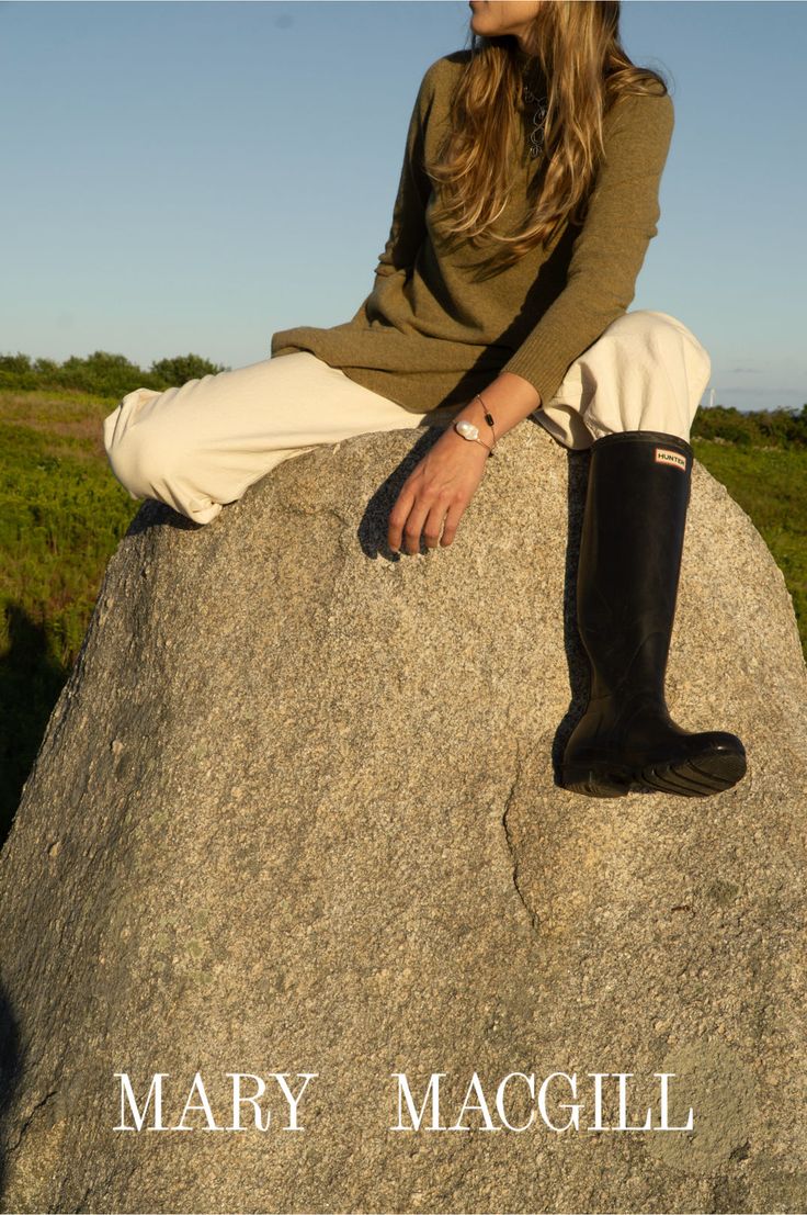Woman with long hair sitting on a large rock outdoors