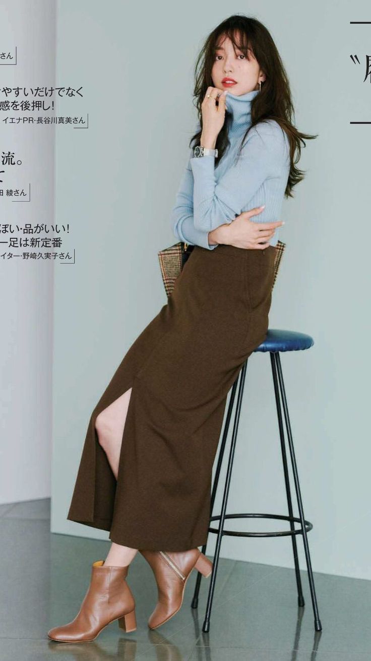 Woman in a light blue turtleneck and brown skirt with a side slit, sitting on a stool