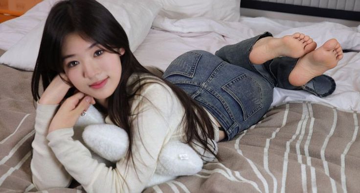 Woman with long dark hair lying on a bed in blue jeans