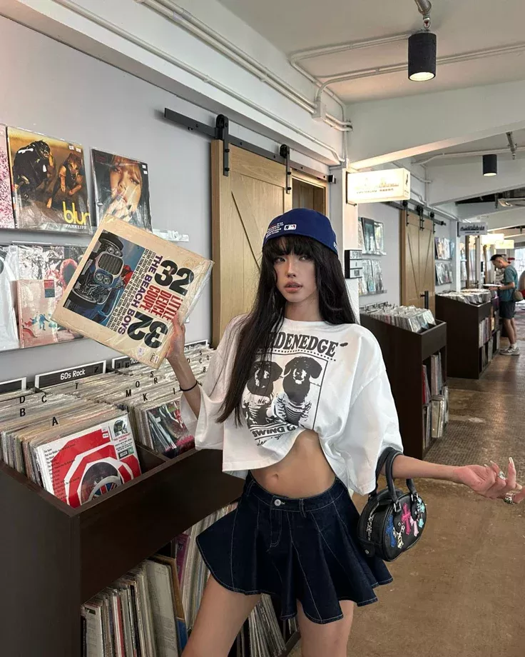 Woman in a crop top and denim skirt holding a record in a record store