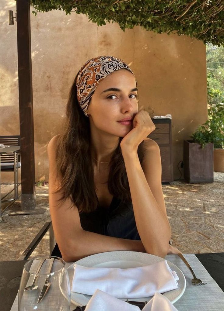 Woman with a patterned headband and long hair sitting outdoors at a table