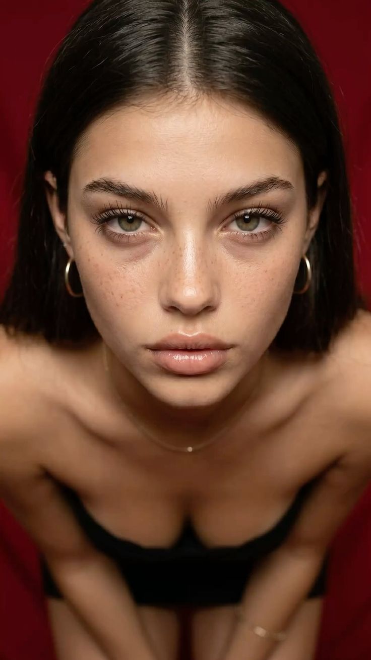 Woman with long dark hair and green eyes against a red background