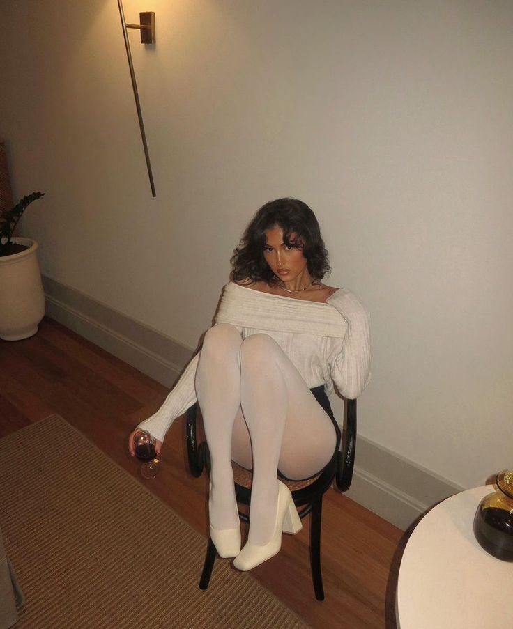 Woman in an off-shoulder top and white tights sitting on a chair indoors