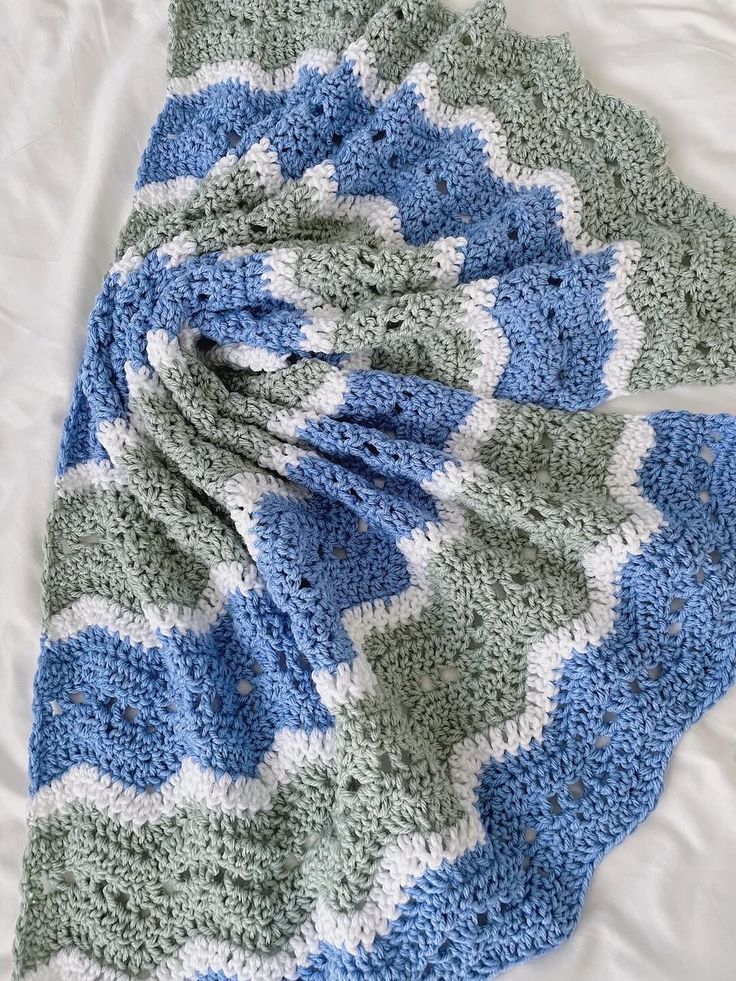 Crochet blanket with blue, green, and white chevron pattern on a white surface
