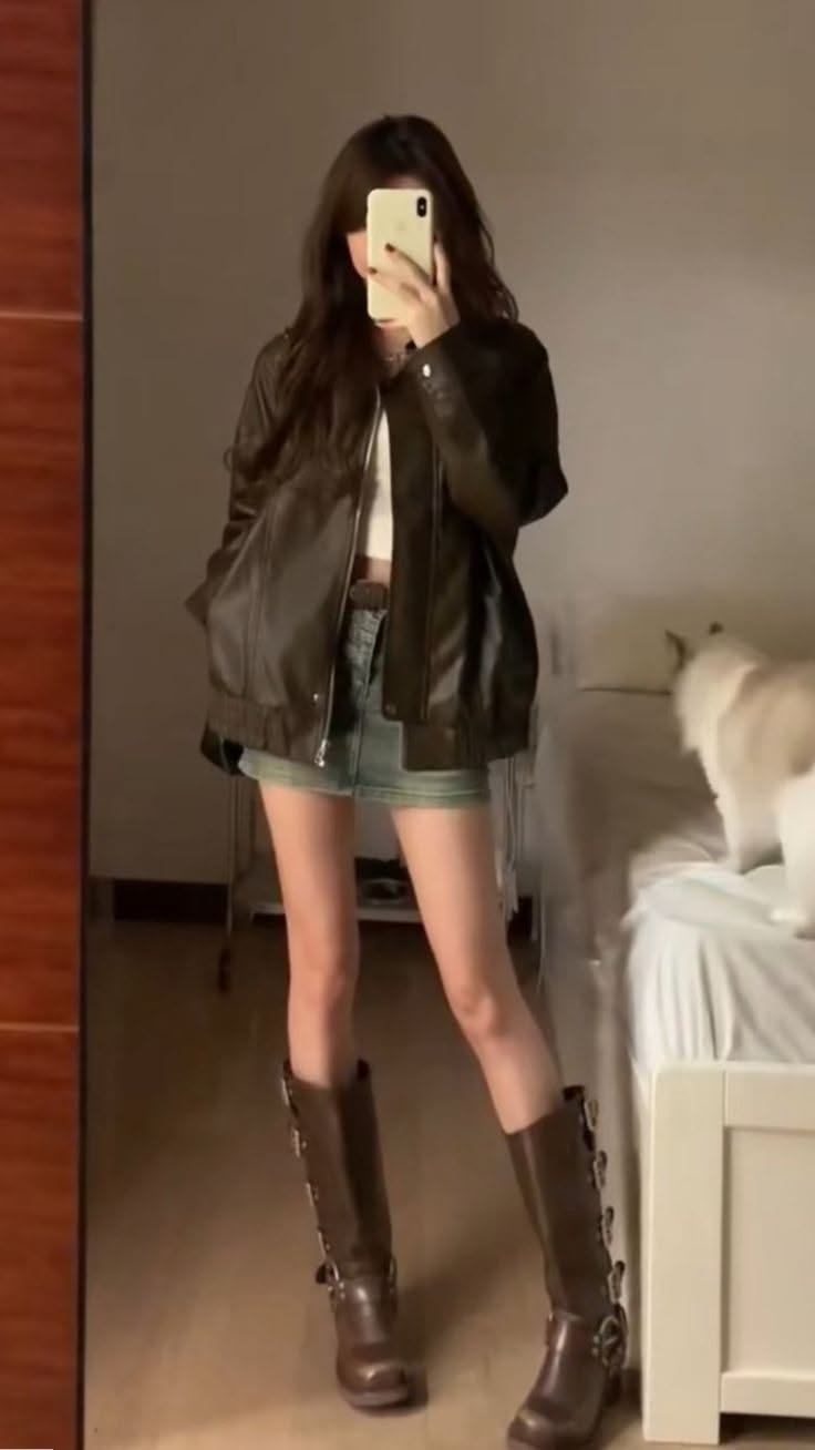 Woman in a leather jacket and denim skirt taking a mirror selfie