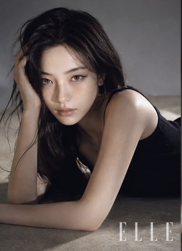 Woman with long dark hair and freckles lying down in a black top