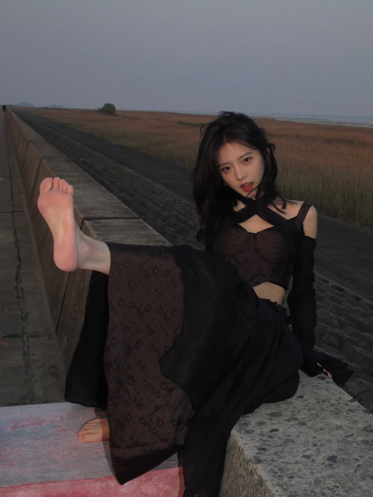 Woman in a black crop top and long skirt posing on a concrete wall at dusk