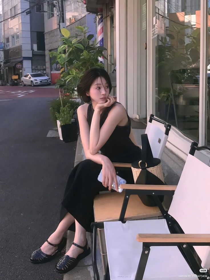 Woman with short hair in a black dress sitting on a chair outdoors