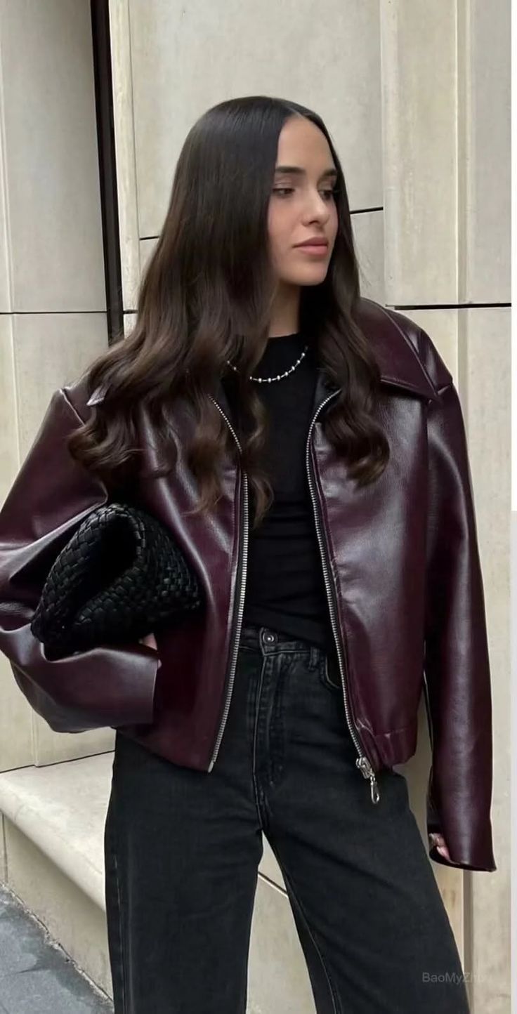 Woman with long dark hair wearing a burgundy leather jacket and black jeans