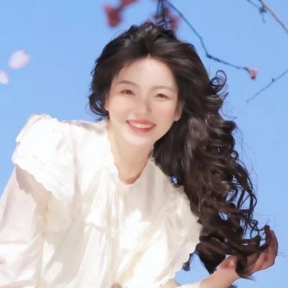 Smiling woman with long dark hair against a blue sky with cherry blossoms