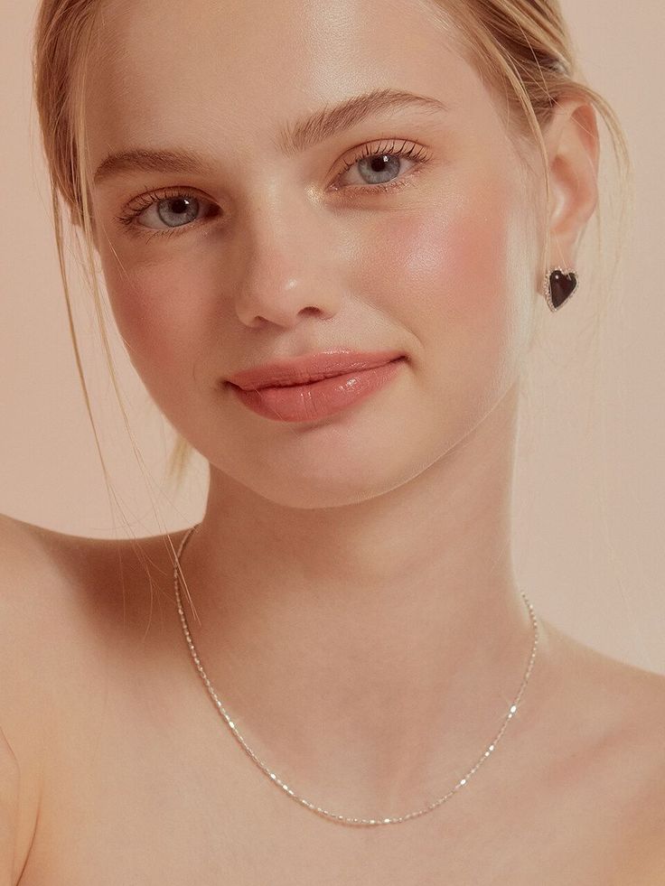 Woman with blonde hair and blue eyes wearing heart earrings and a necklace