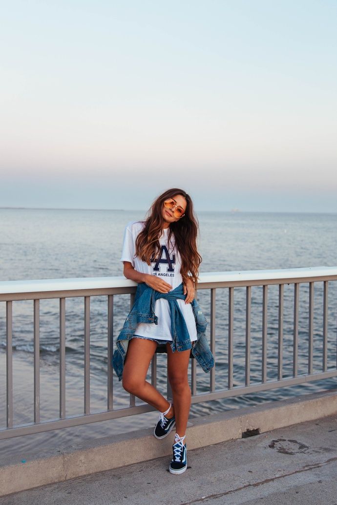Woman in a white t-shirt and denim jacket leaning on a railing by the ocean