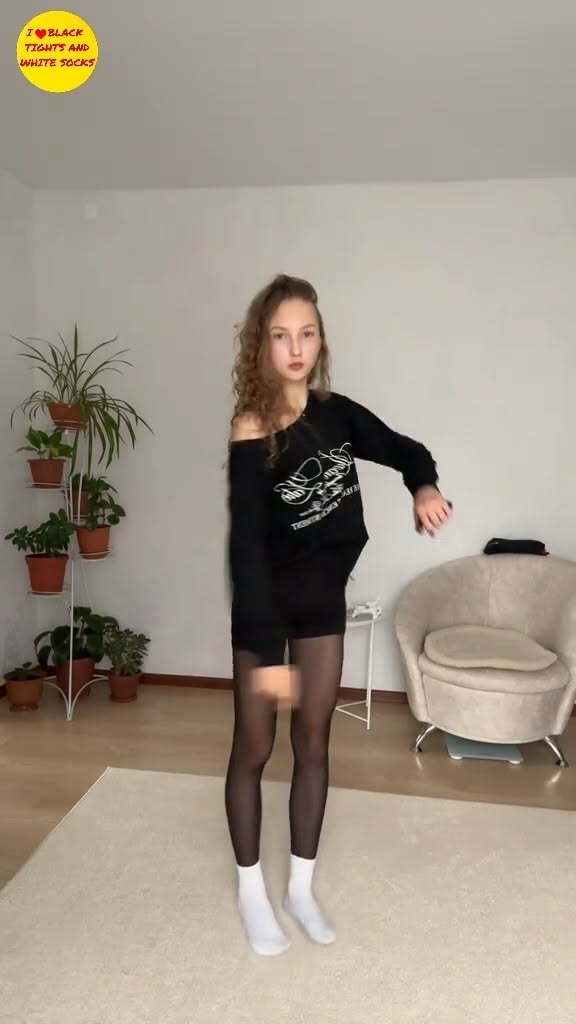 Woman in a black sweatshirt, black tights, and white socks indoors