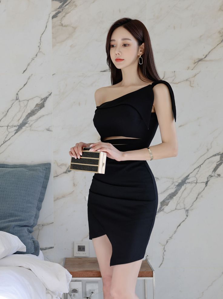 Woman in a black one-shoulder dress with a cut-out waist holding a clutch bag
