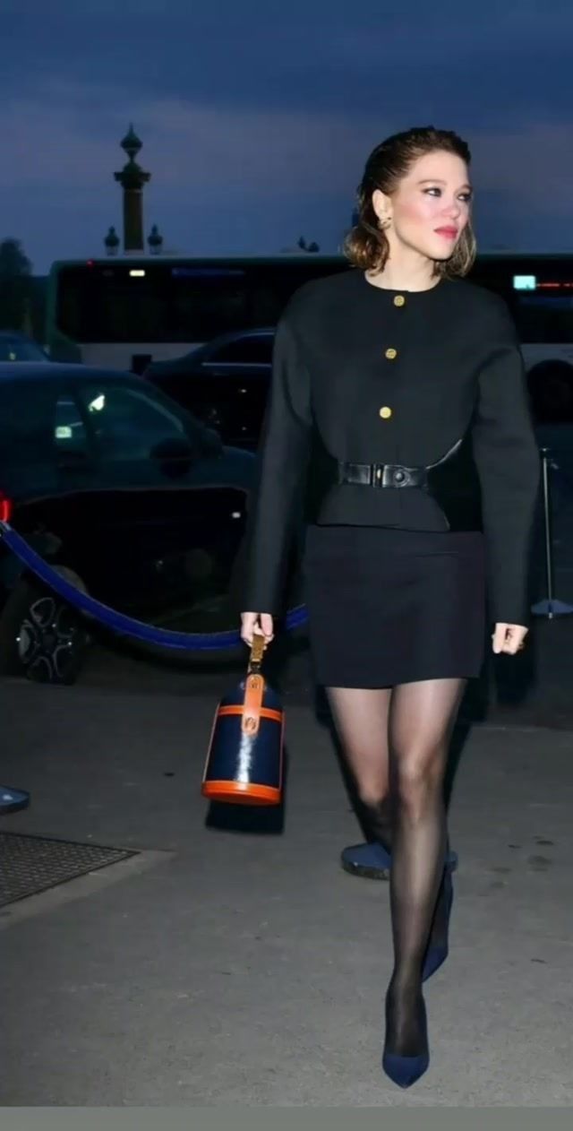 Woman in a black jacket and mini skirt walking outdoors at night