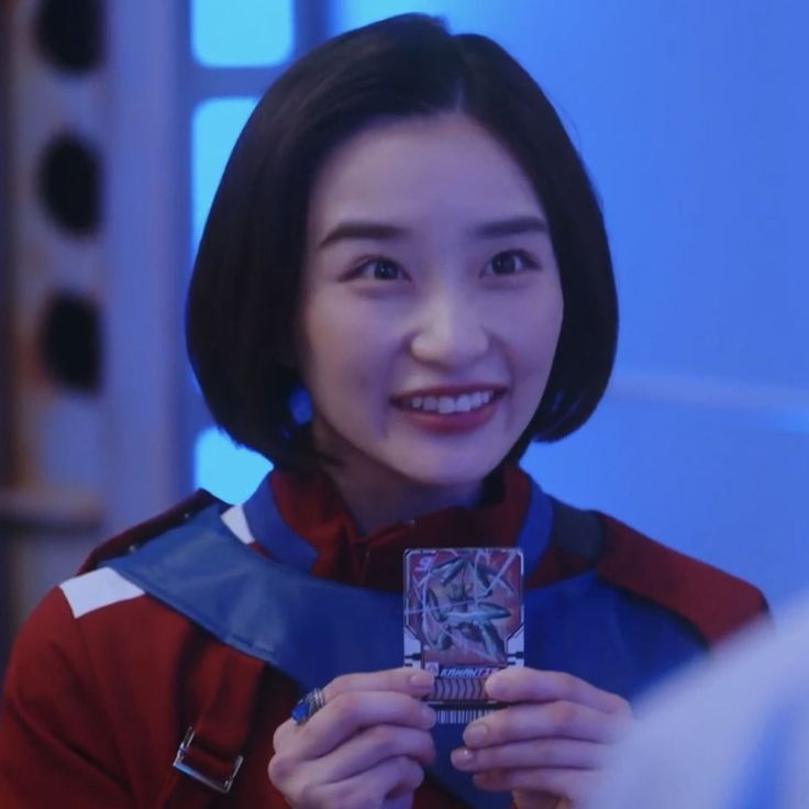 Woman with short hair in a red and blue jacket holding a card