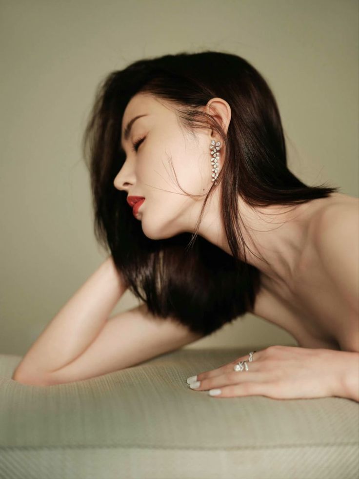 Woman with long dark hair and red lipstick, wearing jewelry and exposed skin
