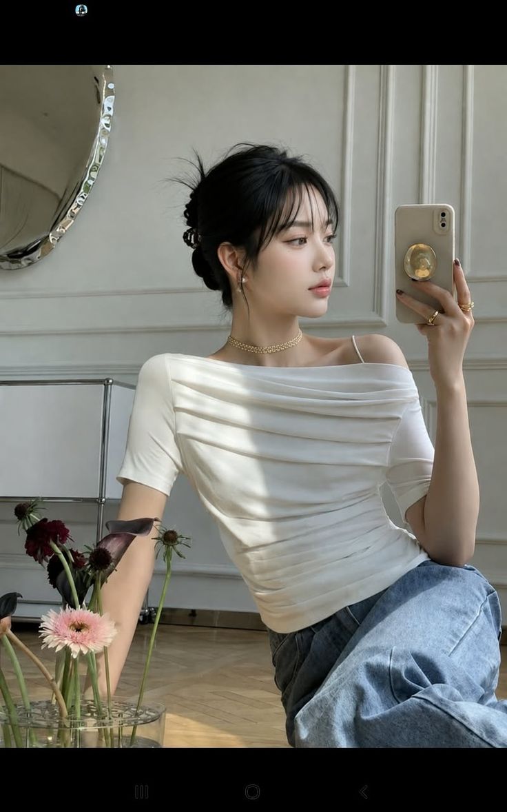 Woman in an off-shoulder top and jeans taking a selfie indoors