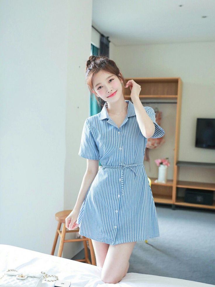 Woman in a blue and white striped dress kneeling on a bed indoors