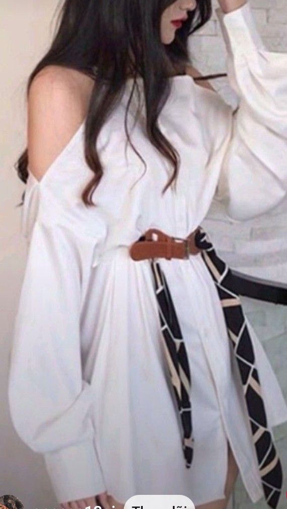 Woman with long dark hair wearing a white off-shoulder dress with a belt and scarf