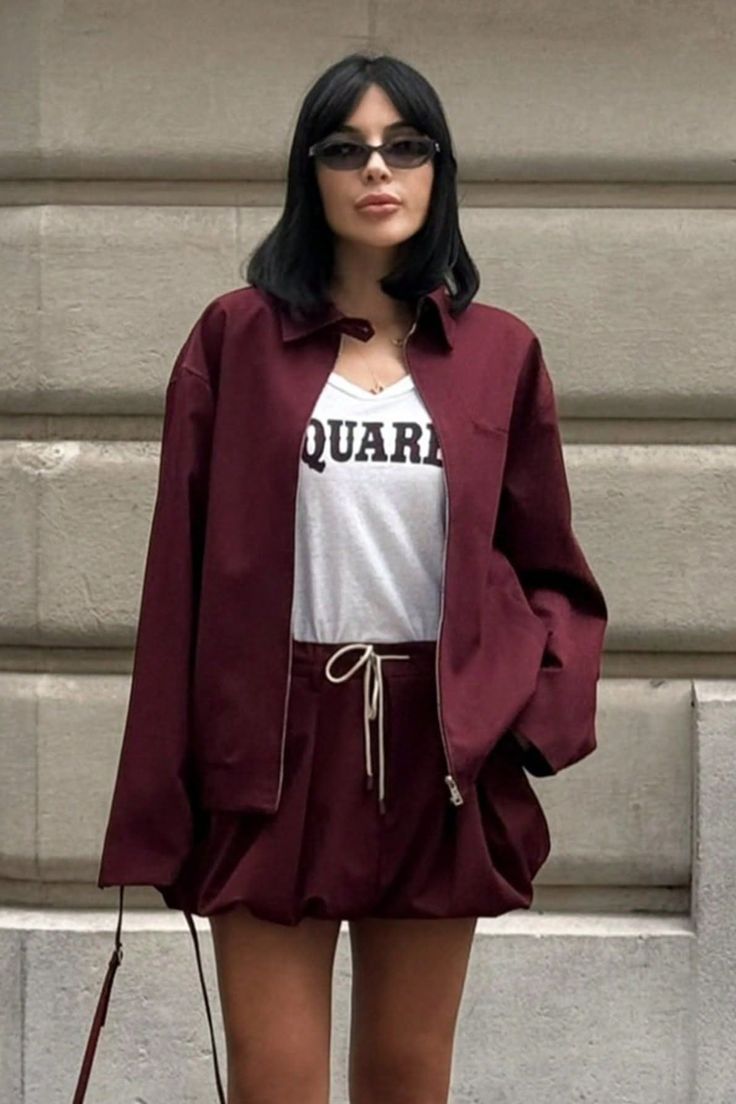 Woman with black hair and sunglasses wearing a maroon jacket and shorts