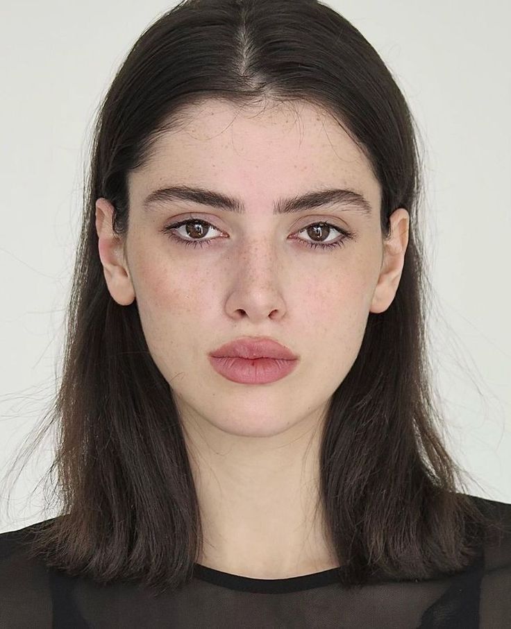 Woman with dark hair and freckles wearing a sheer top, looking directly at the camera