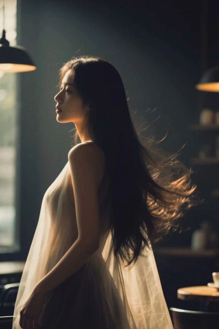 Woman with long hair in a sheer dress, backlit by a window