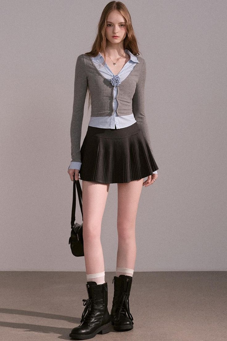 Woman in a pleated skirt, cardigan, and combat boots standing indoors