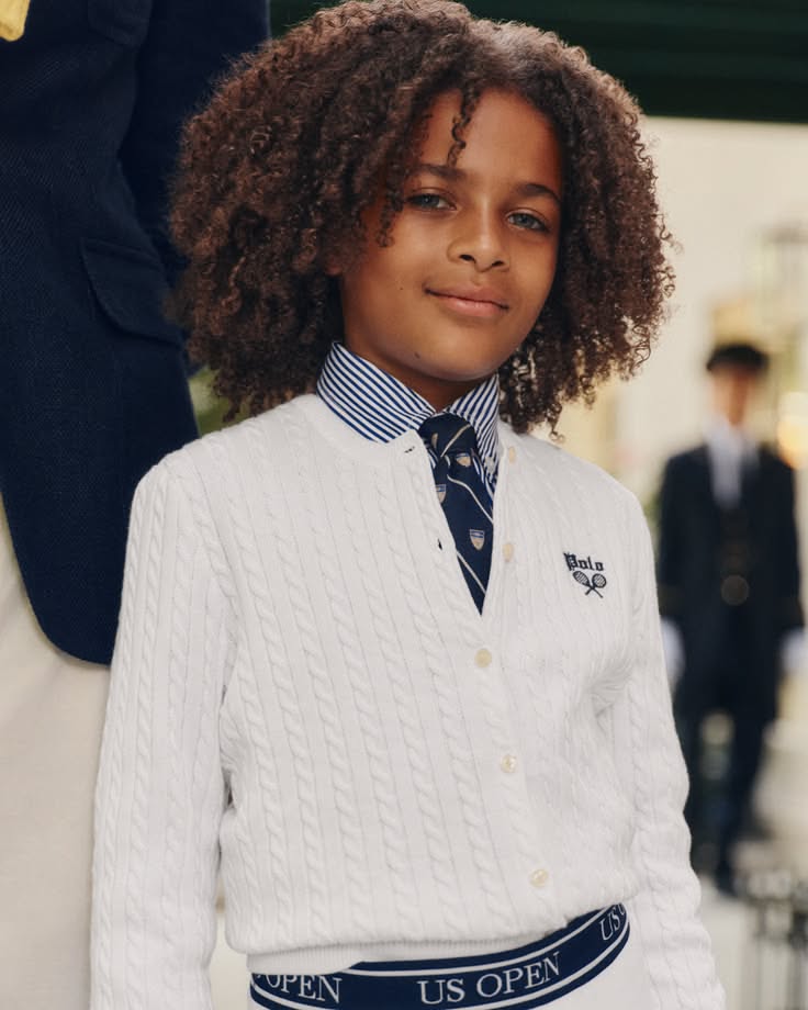 Young boy with curly hair wearing a white cardigan and striped shirt with a tie