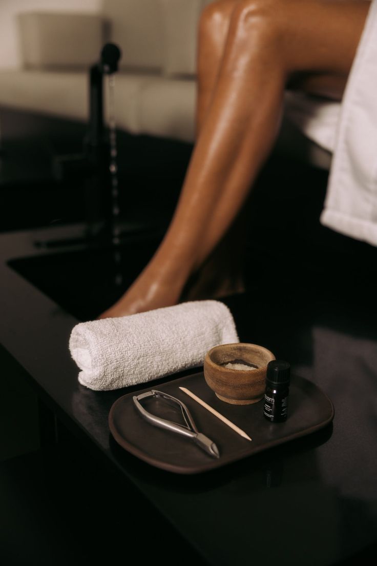 Pedicure tools and essential oil on a tray with a person's legs in the background