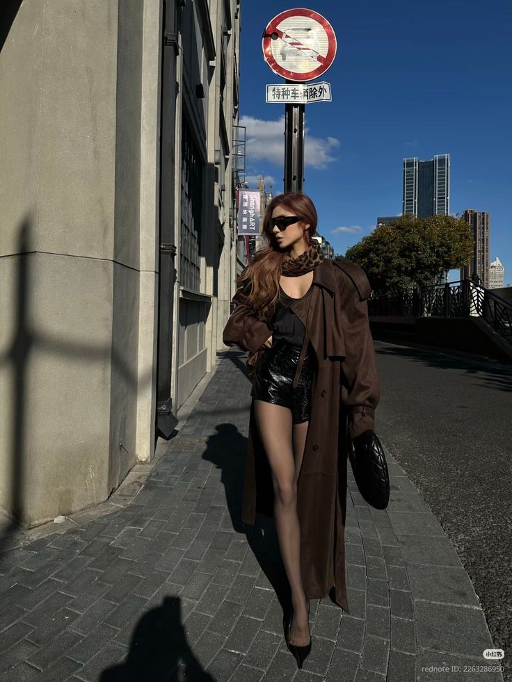 Woman in a brown trench coat and black shorts walking on a city street