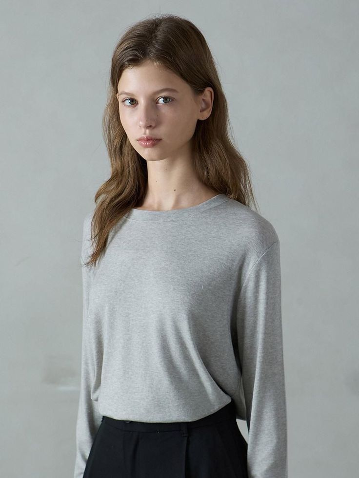 Woman with long brown hair wearing a grey long-sleeve shirt and black pants