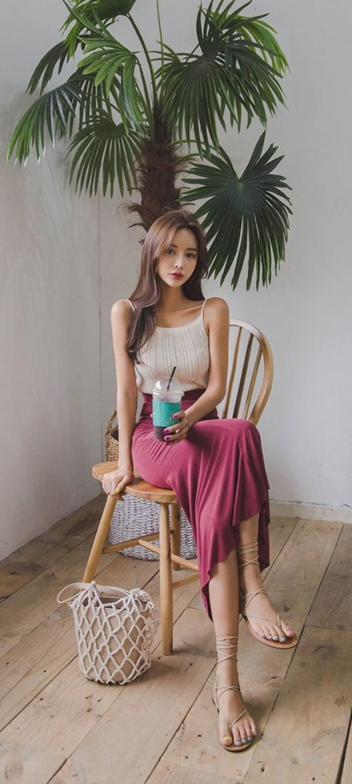 Woman with long hair in a sleeveless top and maxi skirt sitting on a wooden chair