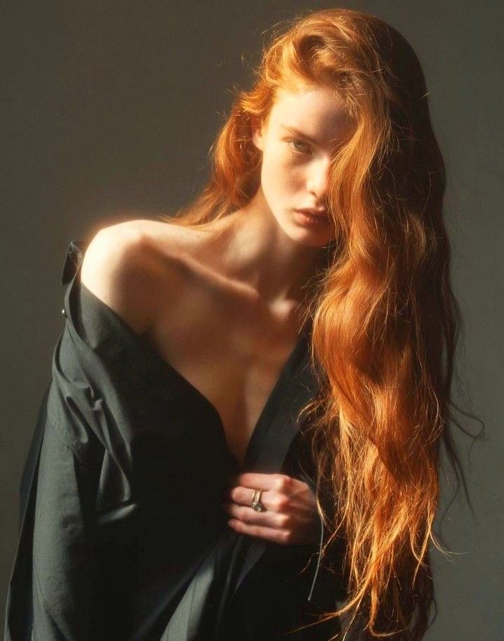 Woman with long red hair in a dark shirt with exposed shoulder and cleavage