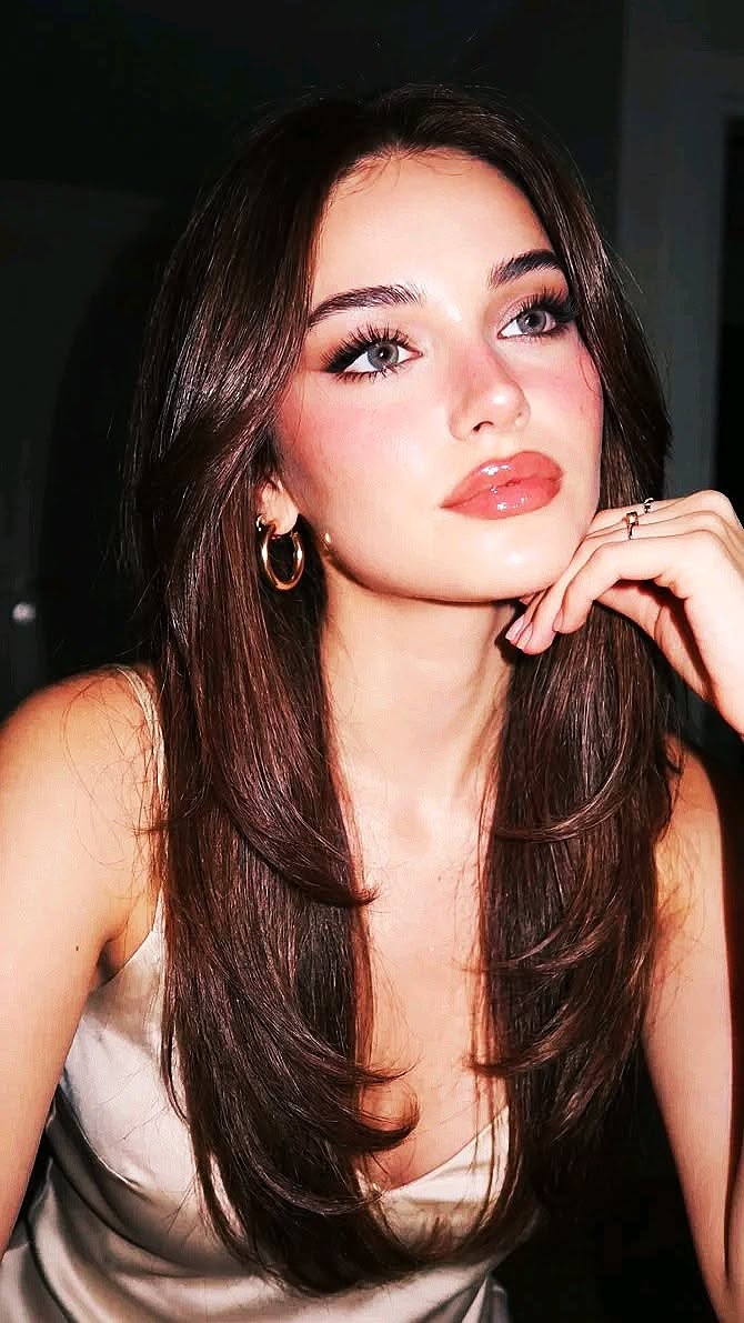 Woman with long brown hair and glossy lips, wearing hoop earrings