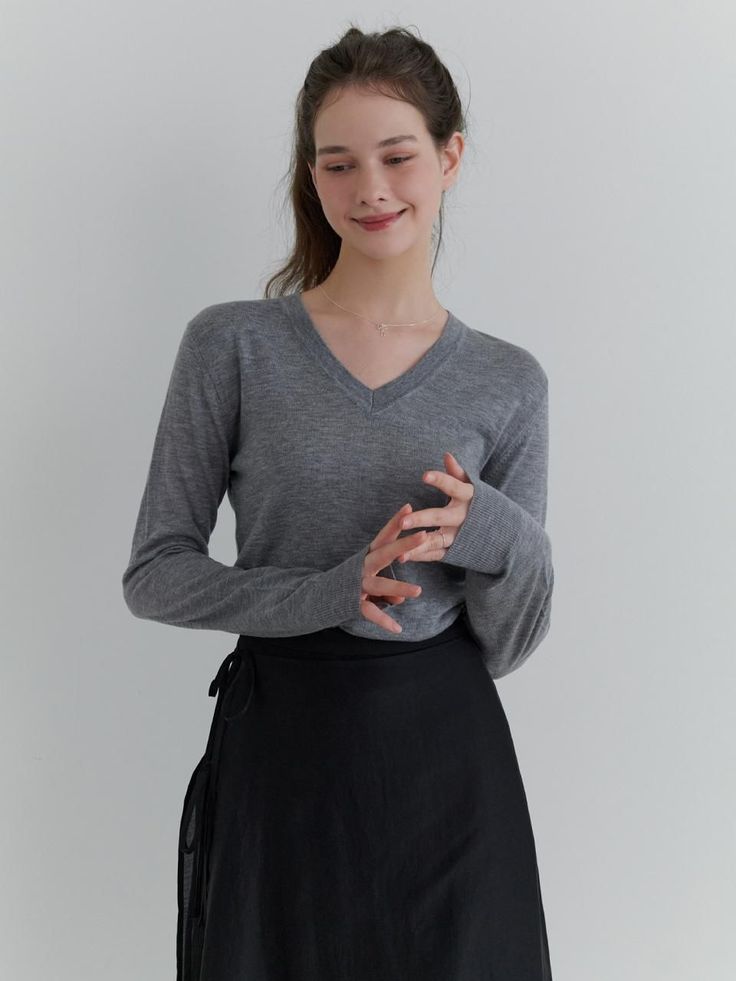 Woman in a gray v-neck sweater and black skirt with a ponytail indoors