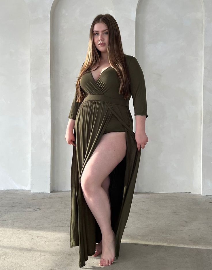 Woman in a green dress with a high slit and cleavage, standing indoors