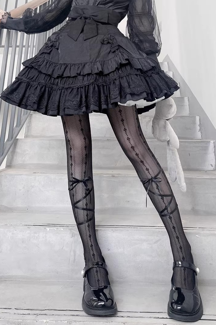 Person in a black ruffled dress and patterned tights with a plush toy on stairs