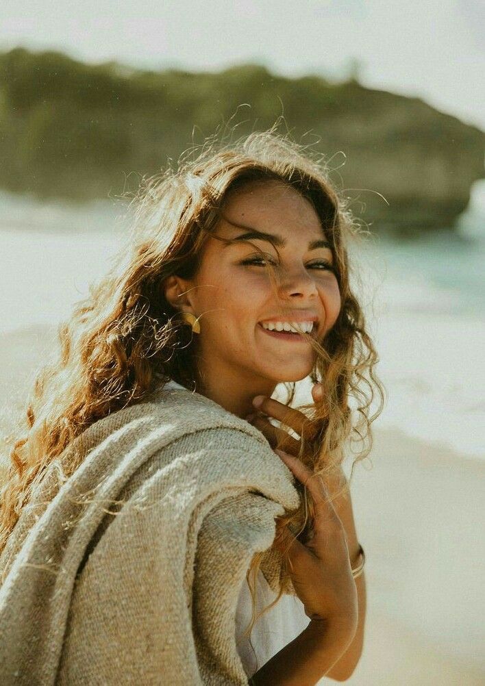 Smiling woman with long curly hair on a beach with soft lighting