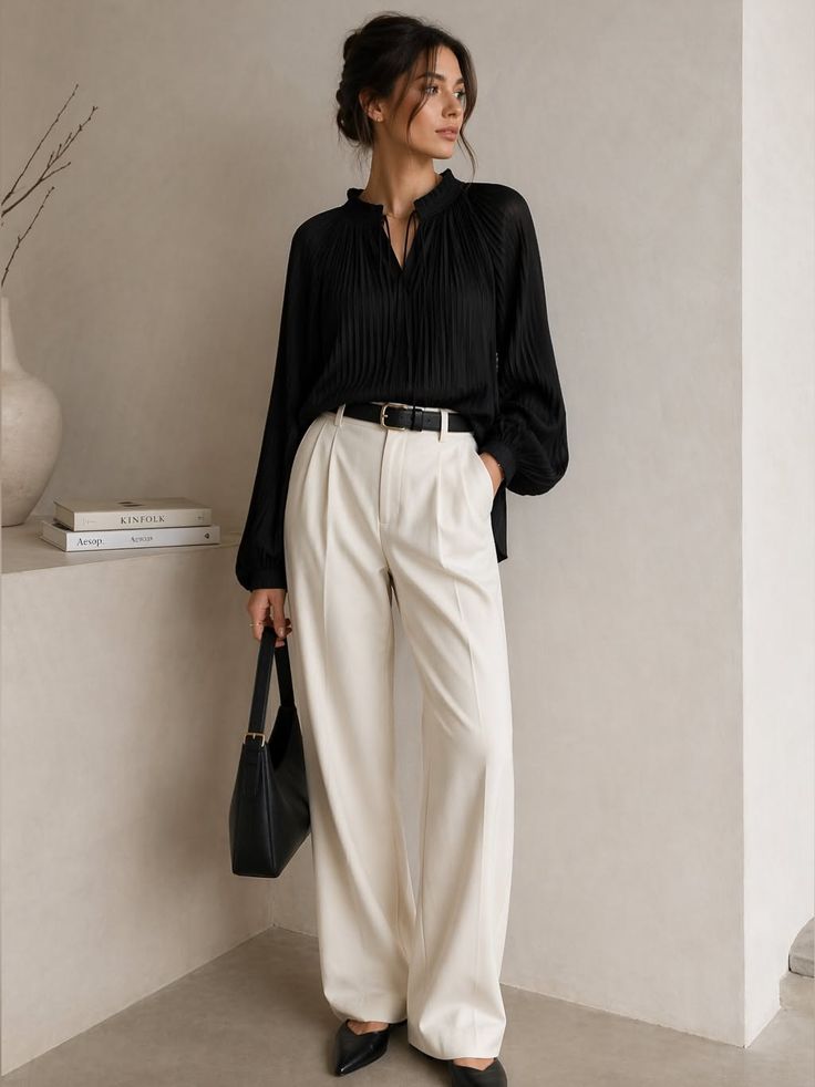 Woman in a black blouse and white wide-leg pants holding a black handbag
