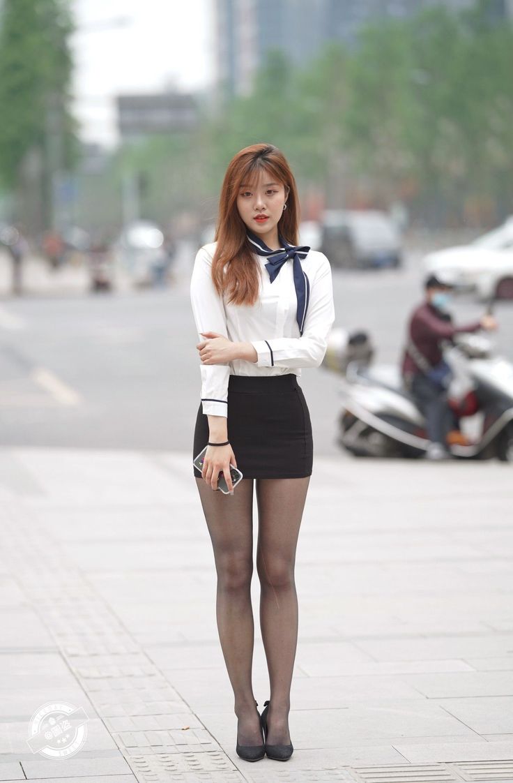 Woman in a white shirt and black mini skirt standing on a street