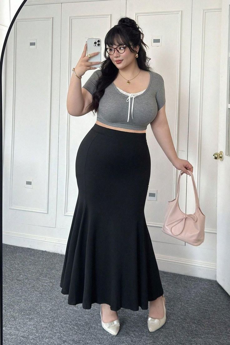 Woman in a gray crop top and black mermaid skirt taking a mirror selfie