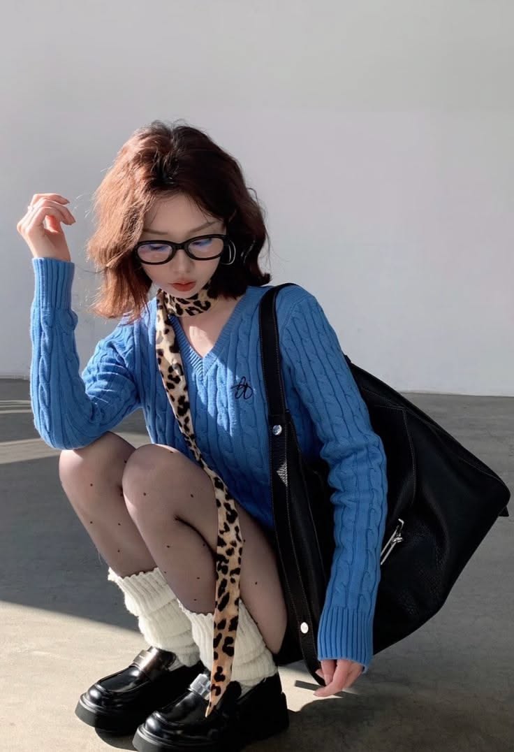 Woman in a blue sweater, glasses, and leopard print scarf squatting indoors