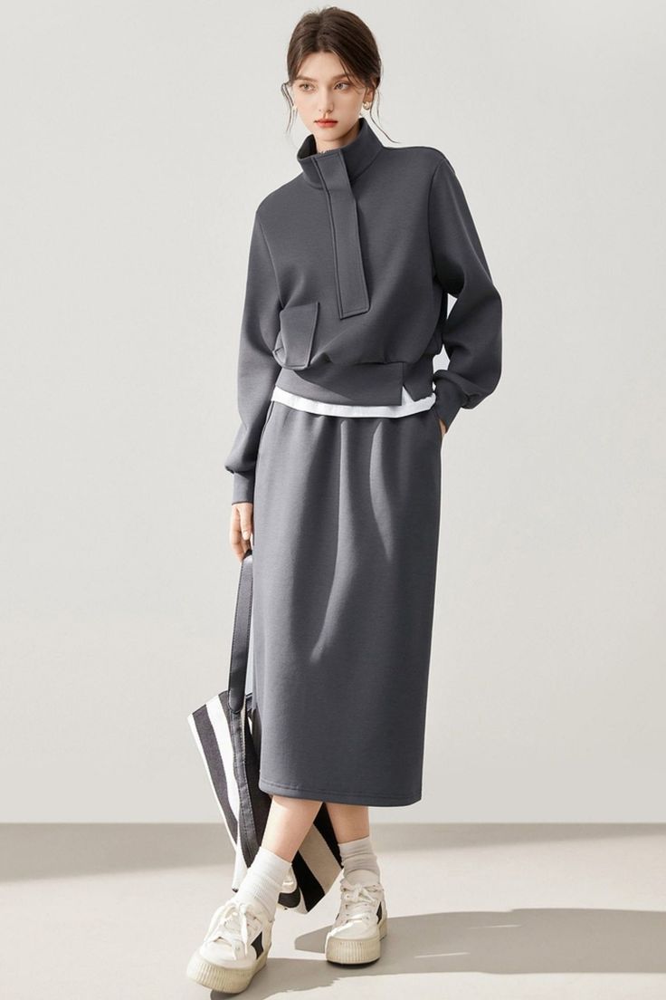 Woman in a gray high-collar top and midi skirt with a striped bag