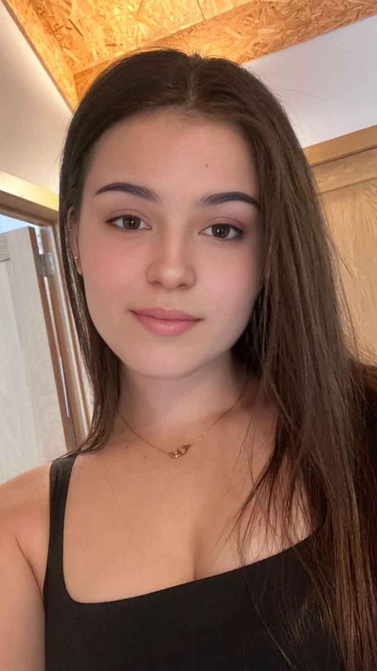 Young woman with long brown hair wearing a black top and gold necklace