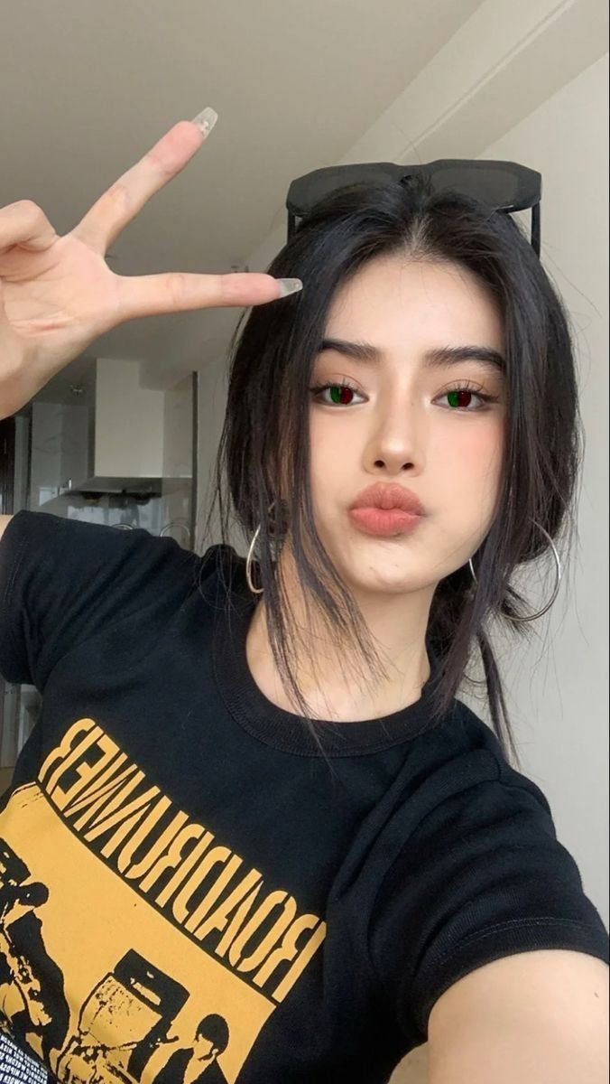 Woman with black hair, red and green eyes, making a peace sign