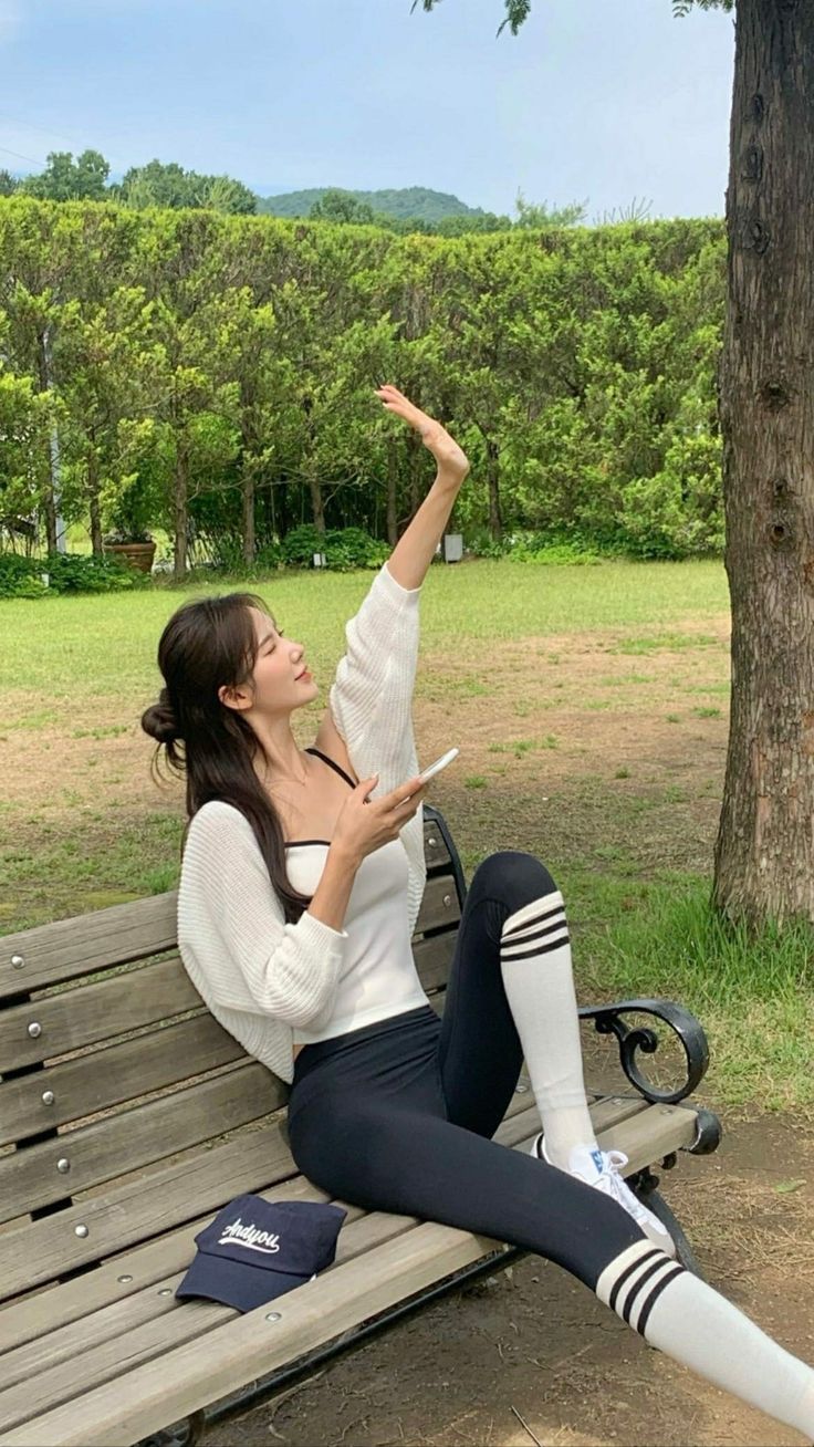 Woman sitting on a park bench with her arm raised, holding a phone
