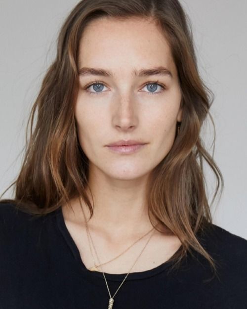 Woman with long brown hair and blue eyes wearing a black shirt and necklaces