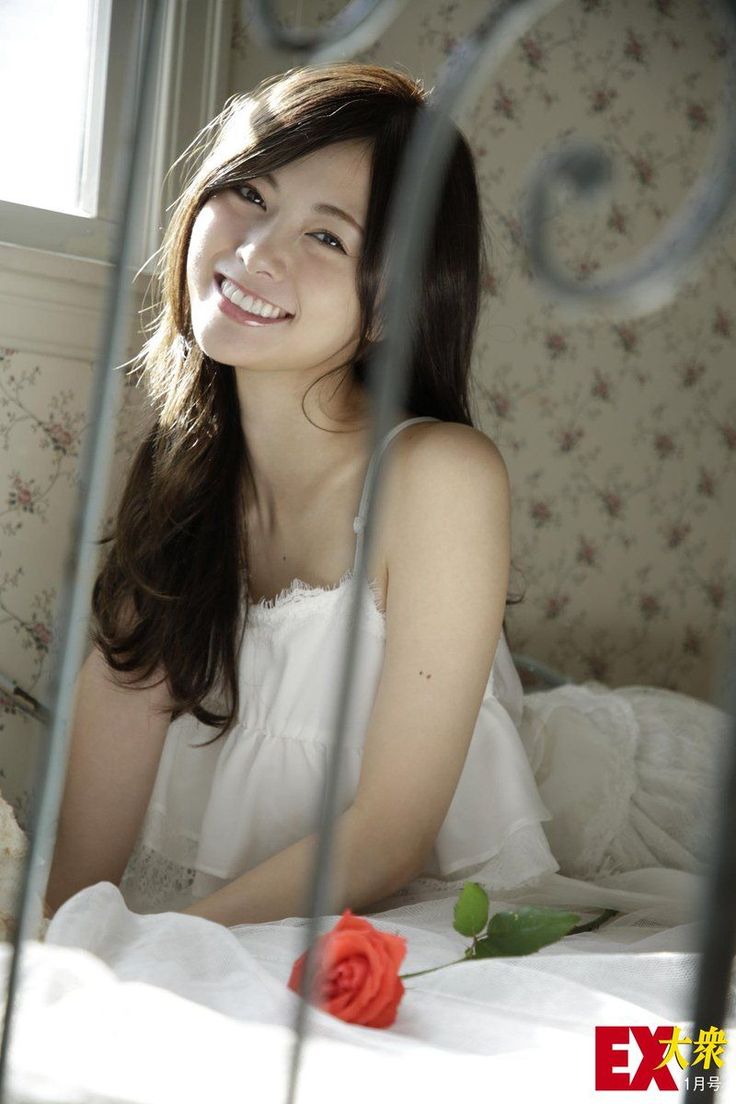 Smiling woman with long hair in a white dress in a sunlit bedroom